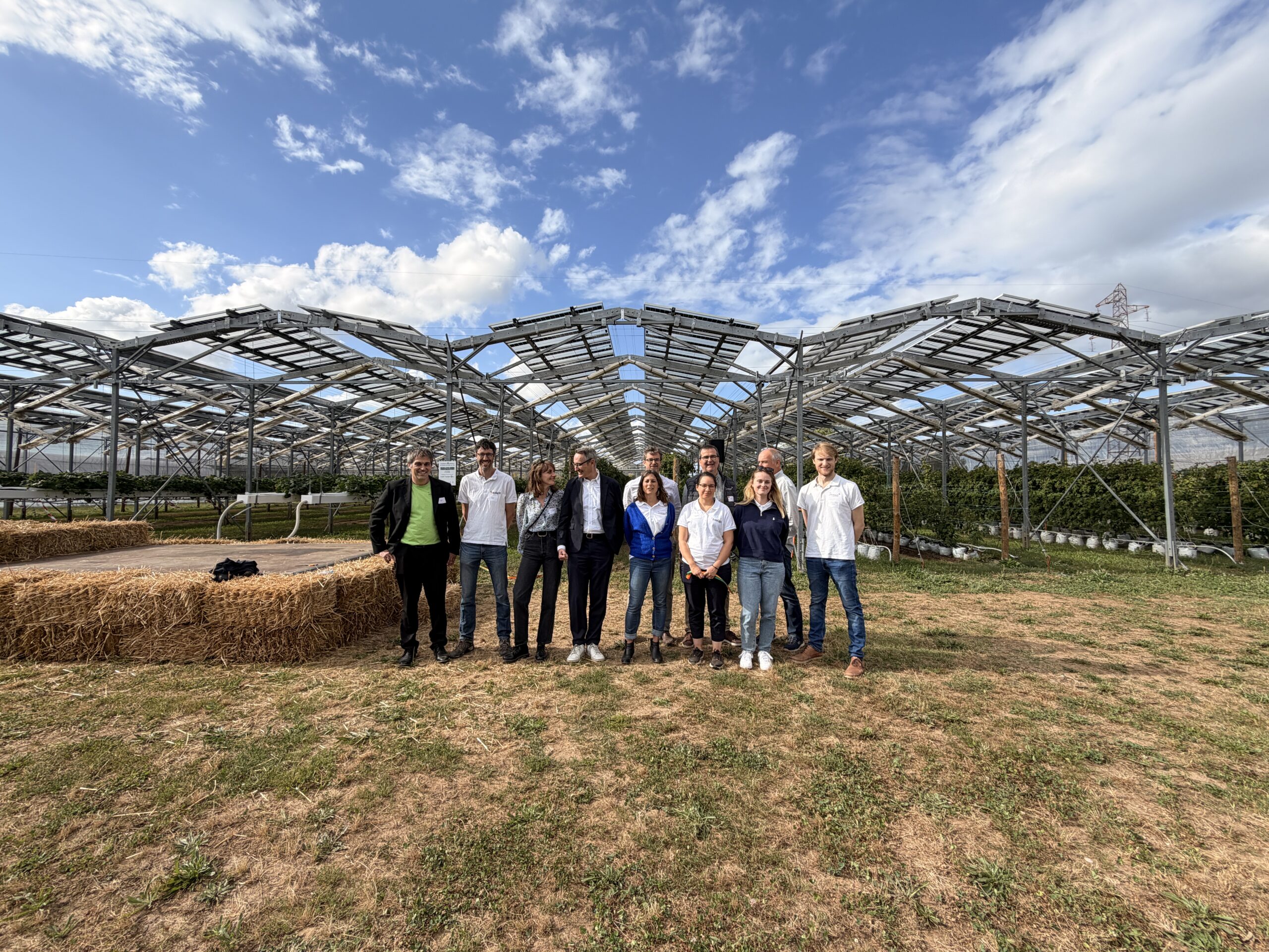 Groupe de participants devant une structure agrivoltaïque lors d’un événement d’inauguration en extérieur.